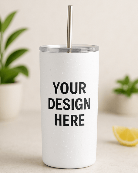White stainless steel tumbler with metal straw featuring the words “Your Design Here,” placed on a neutral surface with plants and a lemon slice in the background.