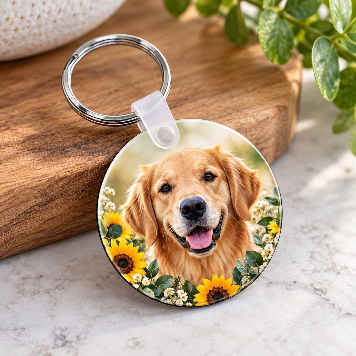 A round custom pet memorial keychain featuring a printed portrait of a golden retriever surrounded by sunflowers, resting on a wooden block over a marble surface.