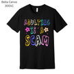 Black graphic T-shirt with bright rainbow text that says ‘Adulting Is a Scam.’ A humorous and relatable gift idea