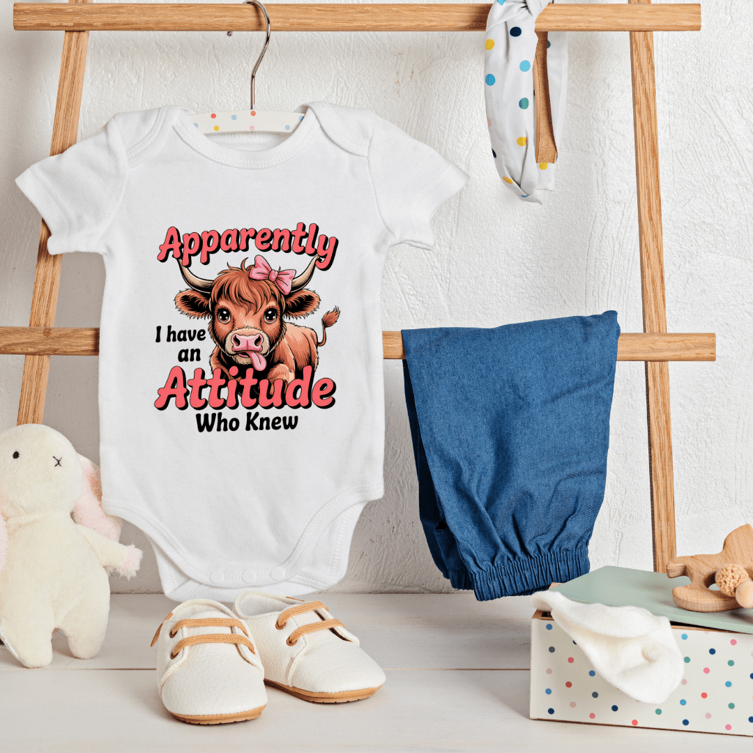 White baby onesie with a cow graphic and text, blue pants, and white shoes on a wooden rack.