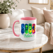 Pink accent Believe alien UFO Bigfoot coffee mug displayed on a table with colourful paranormal themed artwork.