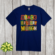 Navy blue t-shirt with 'Black History Month' text in colorful letters on a wooden surface.