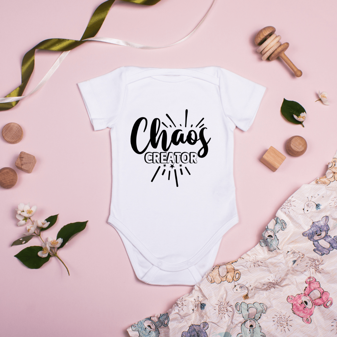 Baby onesie Chaos Creator design styled on pink background with baby toys