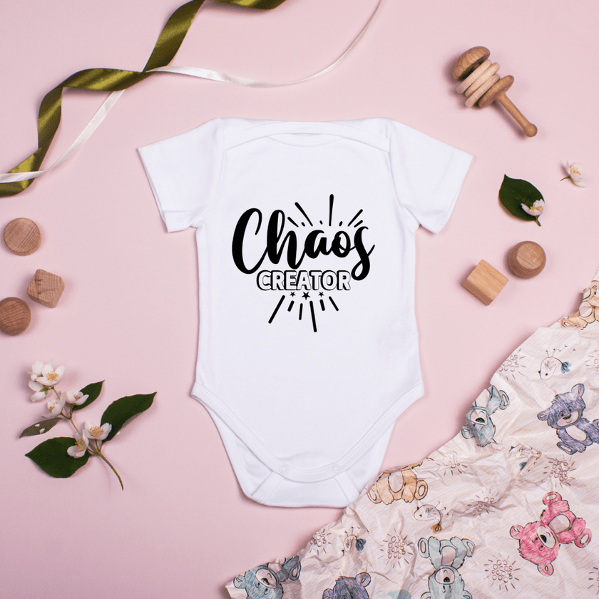 Baby onesie Chaos Creator design styled on pink background with baby toys