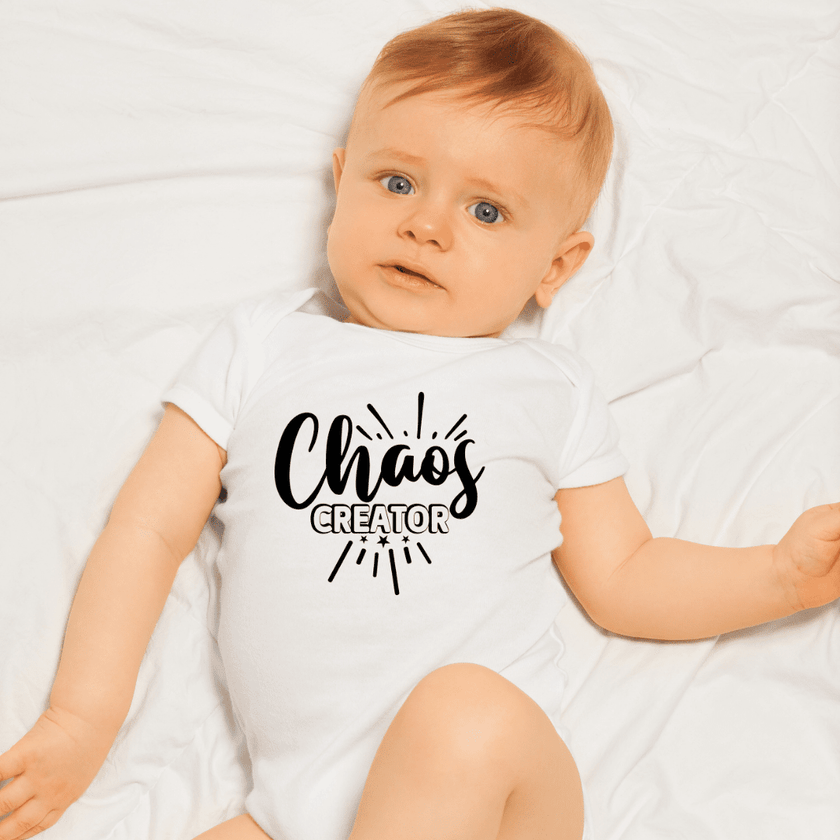 Adorable infant wearing Chaos Creator onesie lying on bed with blue eyes