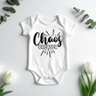 Chaos Creator baby bodysuit displayed flat with eucalyptus leaves and flowers