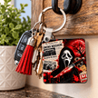 Rectangular horror movie inspired keychain with masked figure, bloody knife, film reel, tickets and popcorn in red and black.