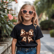 Black youth graphic T shirt with oversized cow print bow design modeled by stylish girl outdoors in natural sunlight