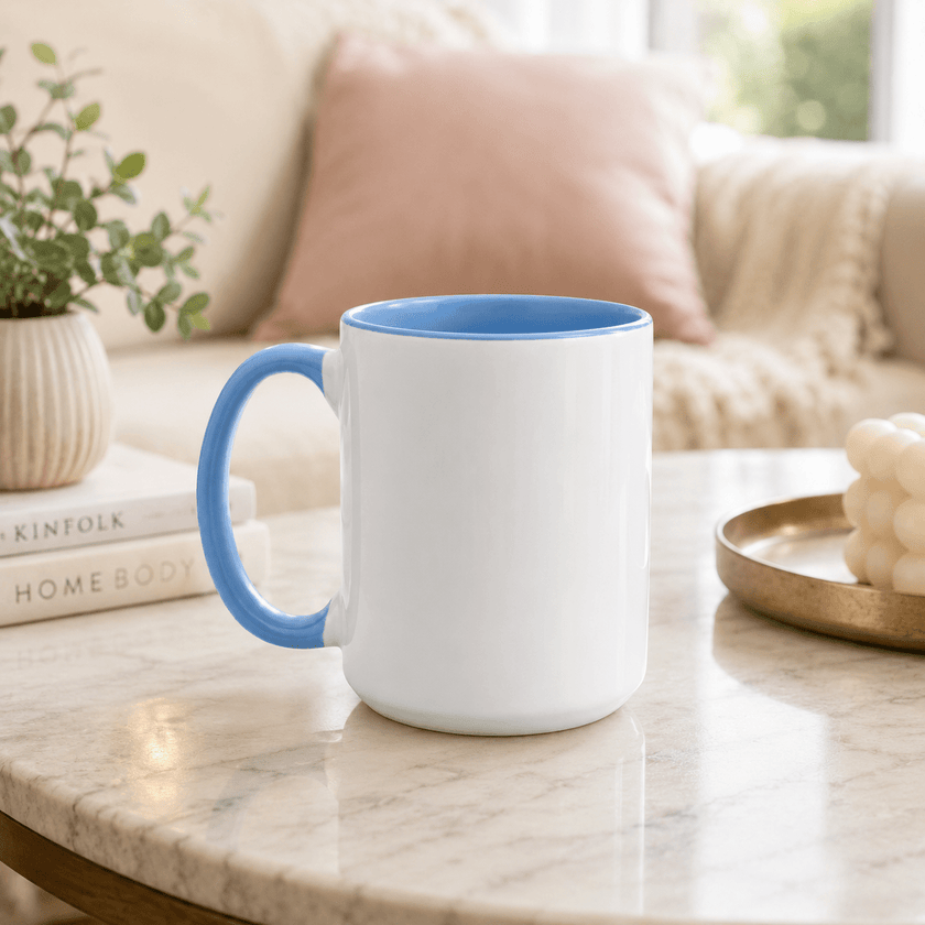 A white ceramic mug with a blue interior and blue handle sits on a marble table in a softly lit living room setting.