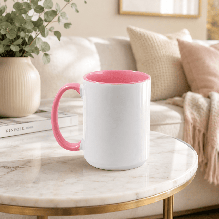 A white ceramic mug with a pink interior and pink handle sits on a round marble-top table in a softly styled living room setting.