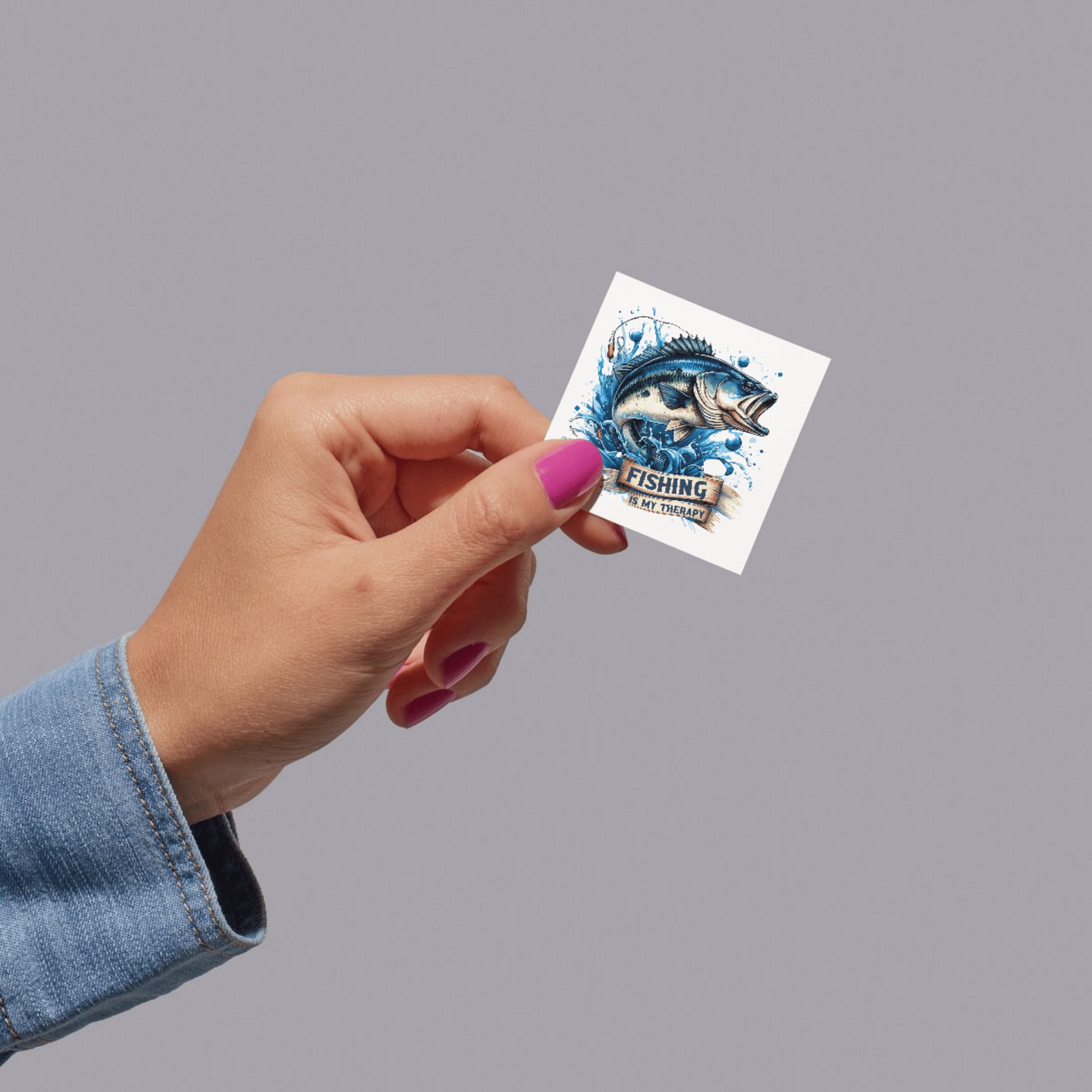 Hand holding a small fishing-themed sticker against a gray background