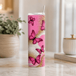 A tall, slim stainless steel tumbler with a clear lid and metal straw, decorated with a pink and gold butterfly pattern, set on a marble countertop in a bright kitchen environment.