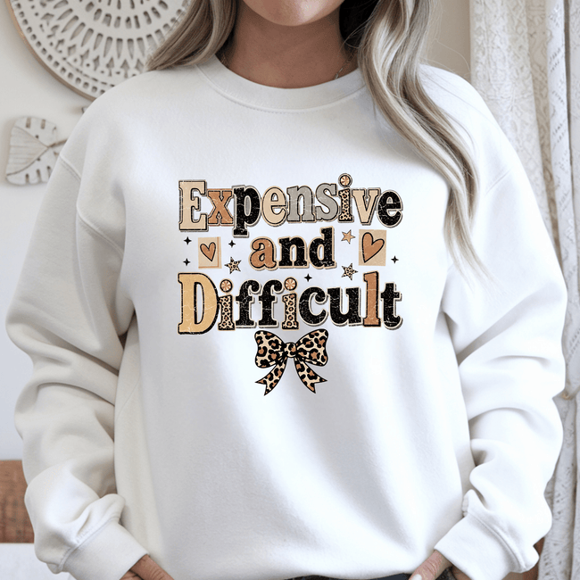 White crewneck sweater displaying Expensive and Difficult typography graphic with leopard bow and trendy women's casual fashion style.