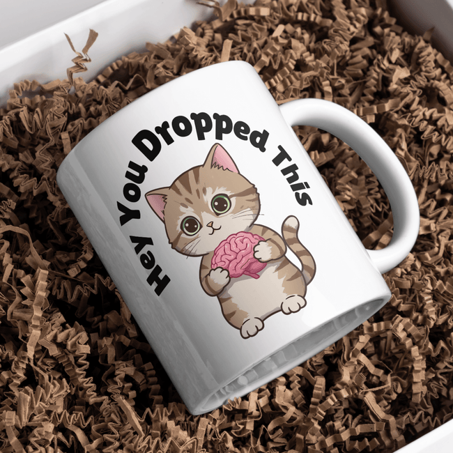Cute cat holding a brain on a ceramic mug with text “Hey You Dropped This.”