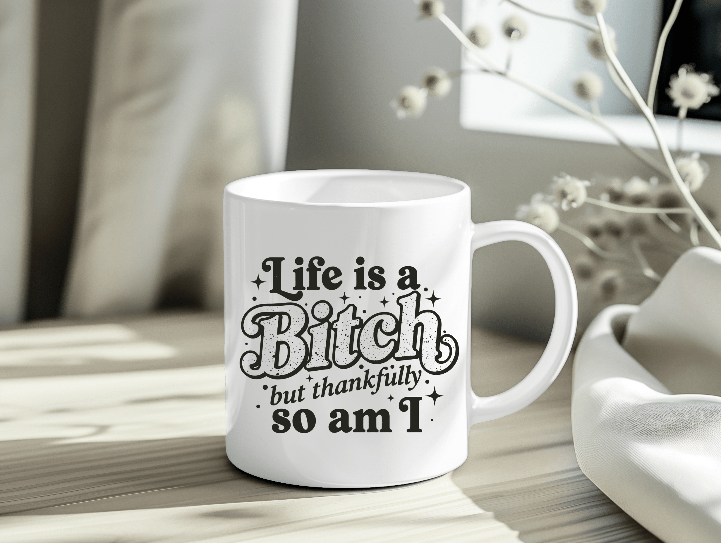White ceramic mug with the quote “Life Is a Bitch but Thankfully So Am I” in bold black typography.