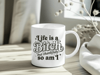 White ceramic mug with the quote “Life Is a Bitch but Thankfully So Am I” in bold black typography.