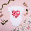 Cute Valentine’s Day baby bodysuit displayed on flat background