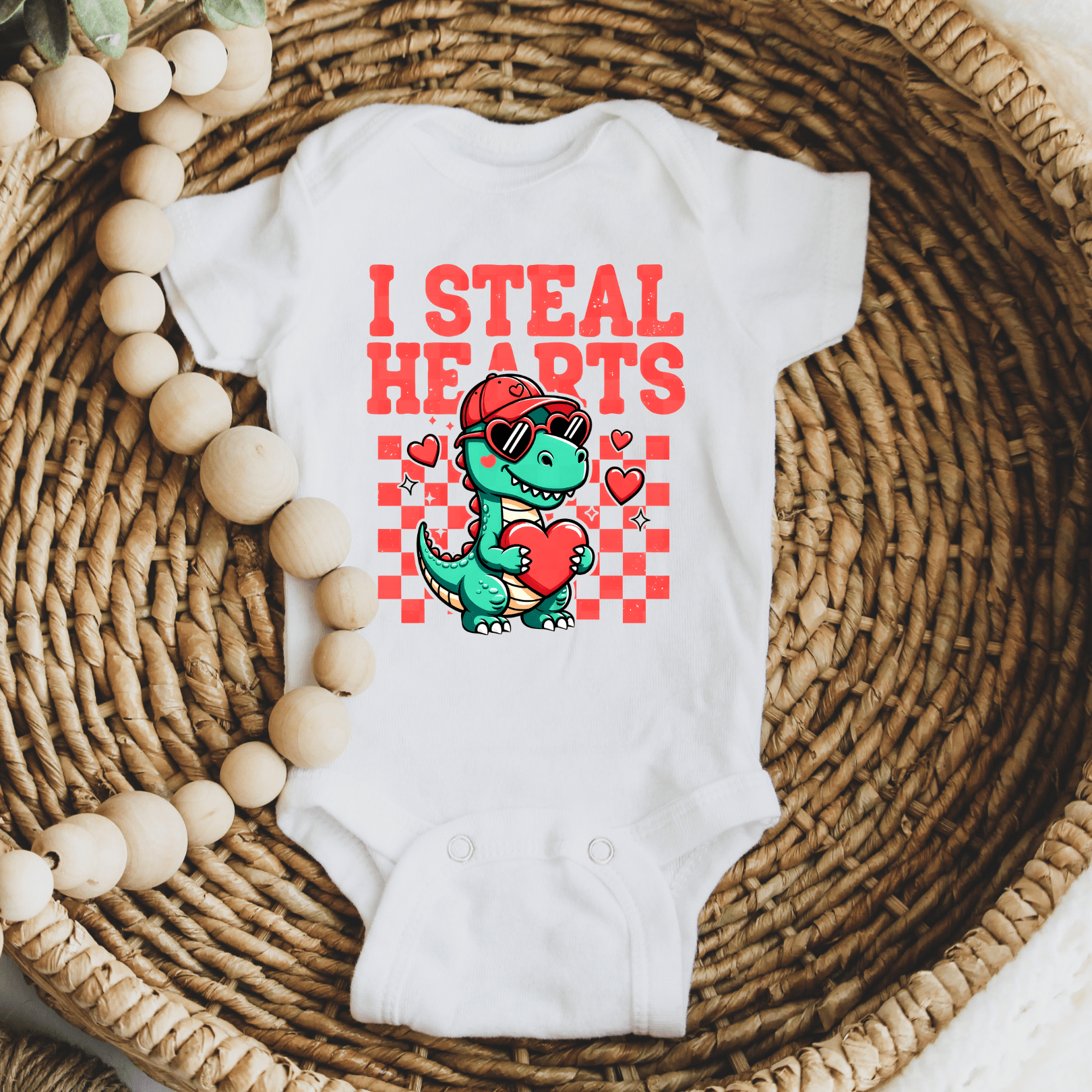 White baby onesie with I Steal Hearts dinosaur graphic laid flat