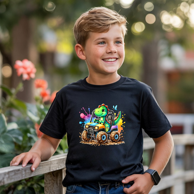 Boys black youth tee with bright dinosaur monster truck artwork, mud tires, and playful splatter accents.