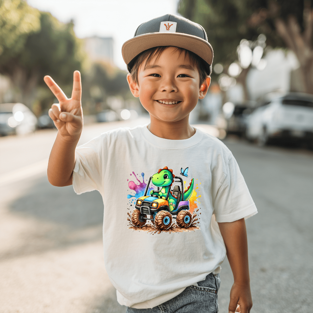 White t-shirt  kids graphic T shirt with a cheerful green dinosaur driving a colorful monster truck design.