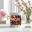 Floral MOM mug displayed on table with soft background flowers and natural lighting