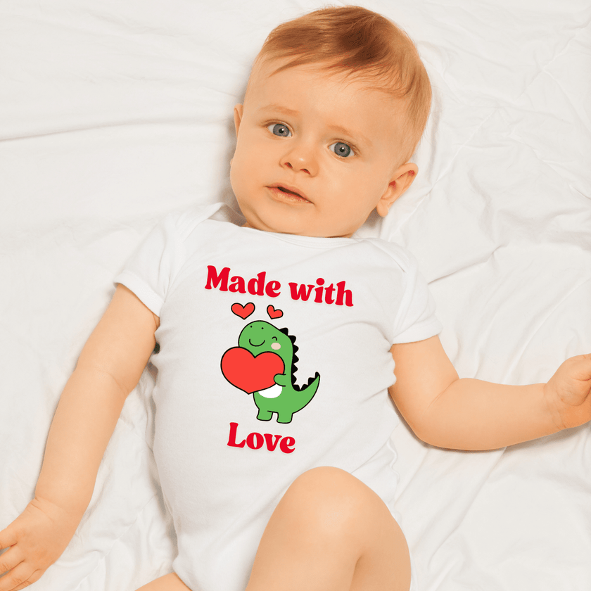 Baby wearing a white onesie with a dinosaur and heart design, laying on a white blanket.