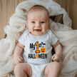 Smiling baby wearing a white My First Halloween baby onesie with orange pumpkin, bat and spiderweb graphic.