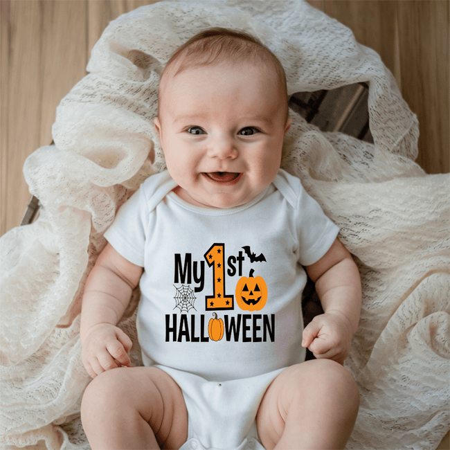 Smiling baby wearing a white My First Halloween baby onesie with orange pumpkin, bat and spiderweb graphic.