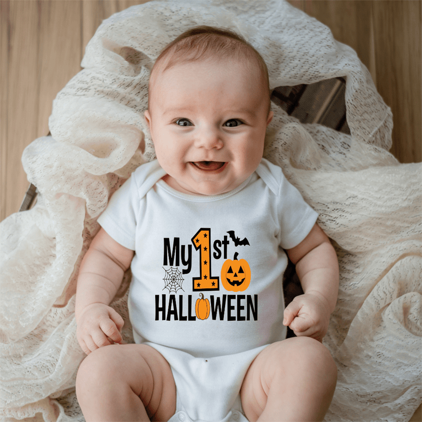 Smiling baby wearing a white My First Halloween baby onesie with orange pumpkin, bat and spiderweb graphic.