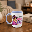 A white ceramic coffee mug with a light blue handle and interior, featuring a graphic of a woman in a purple headscarf and pink shirt next to the text 'OH LOOK! NOBODY gives a SHIT'. The mug is placed on a wooden table in a cozy living room setting with books and a sofa in the background.