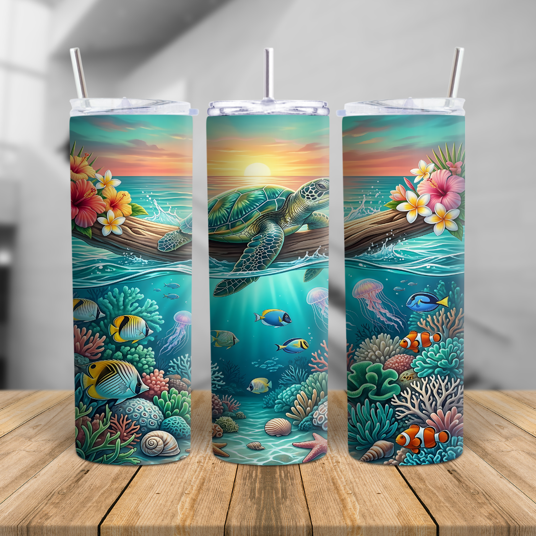 Sea turtle skinny tumbler cup featuring a tropical sunset, coral reef, fish, shells, and ocean artwork, shown on a beach with a clear lid and metal straw.
