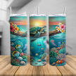 Sea turtle skinny tumbler cup featuring a tropical sunset, coral reef, fish, shells, and ocean artwork, shown on a beach with a clear lid and metal straw.