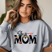 Grey crewneck sweater worn in lifestyle setting featuring She Is Mom affirmation design