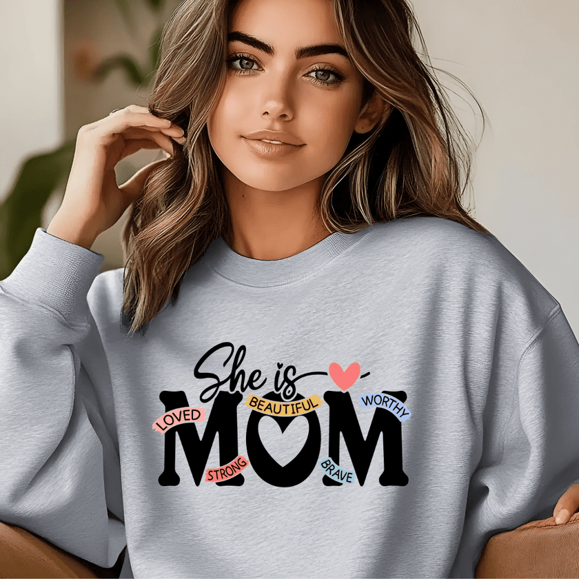 Grey crewneck sweater worn in lifestyle setting featuring She Is Mom affirmation design