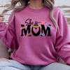 Pink crewneck sweater with “She Is Mom” inspirational graphic featuring words loved strong beautiful worthy brave