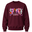 A maroon crewneck sweatshirt featuring a colorful 'Spooky Vibes' graphic on the chest with Halloween-themed illustrations.