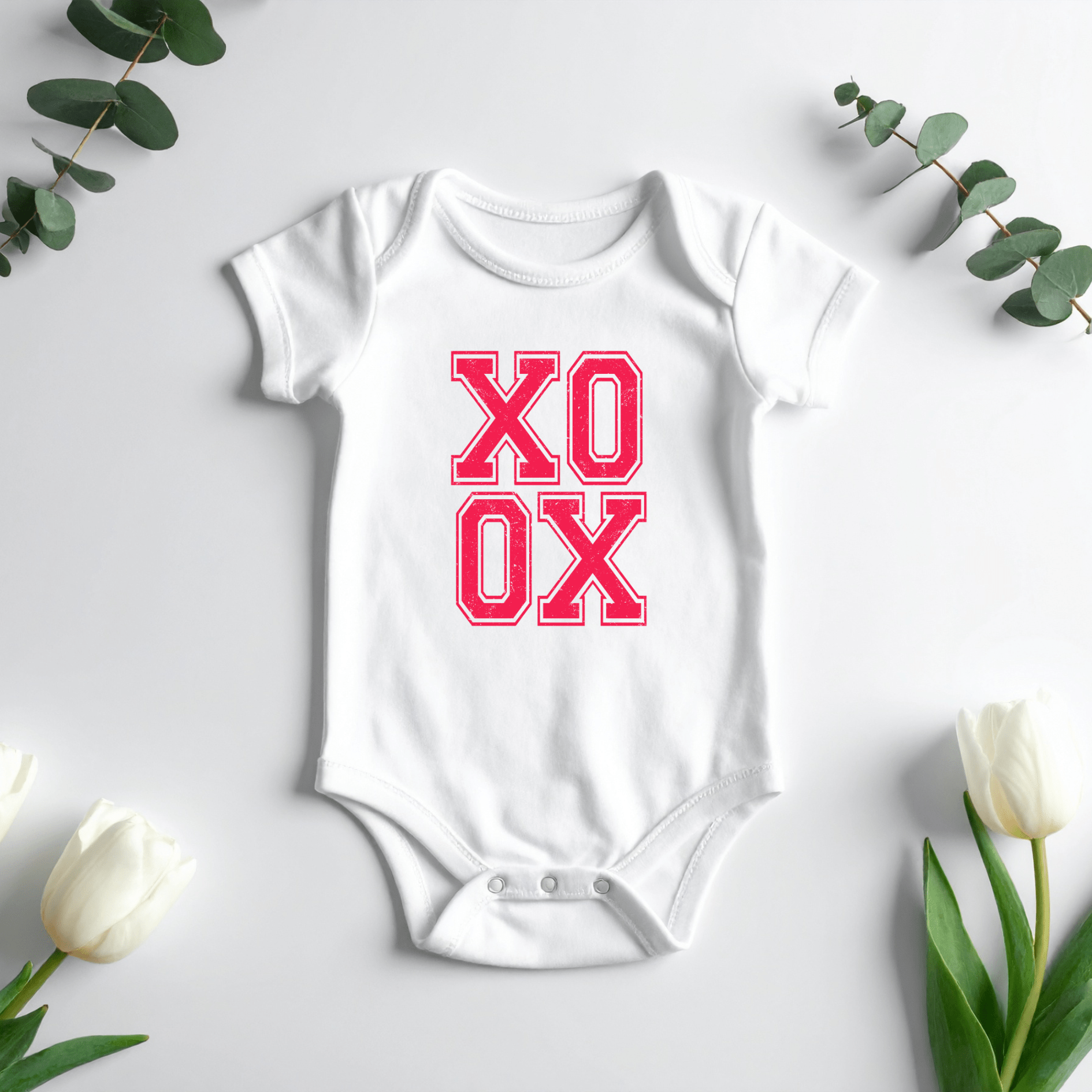 Newborn baby XO XO onesie surrounded by eucalyptus leaves and tulips