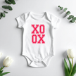 Newborn baby XO XO onesie surrounded by eucalyptus leaves and tulips